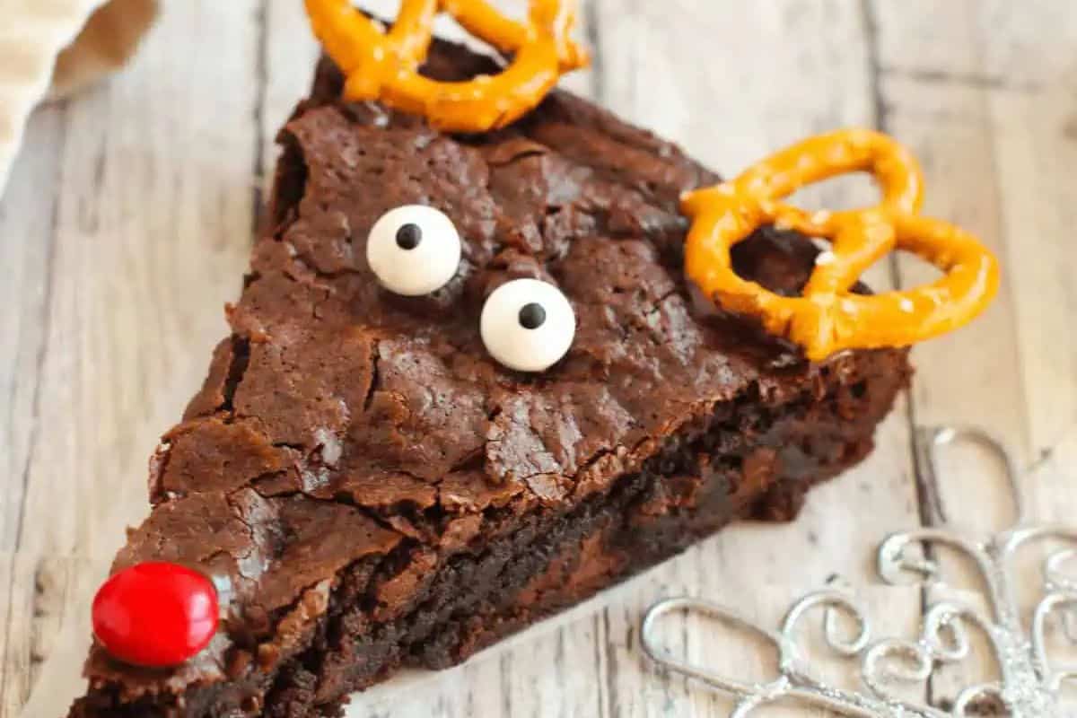 Chocolate brownie decorated with pretzel antlers, candy eyes, and a red nose to look like reindeer.