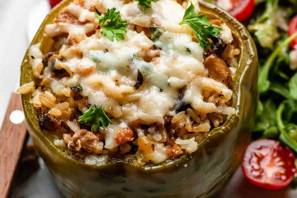 A close-up of an easy stuffed pepper filled with rice, vegetables, and melted cheese, garnished with parsley, with salad and cherry tomatoes on the side—perfect for simple weeknight dinners.