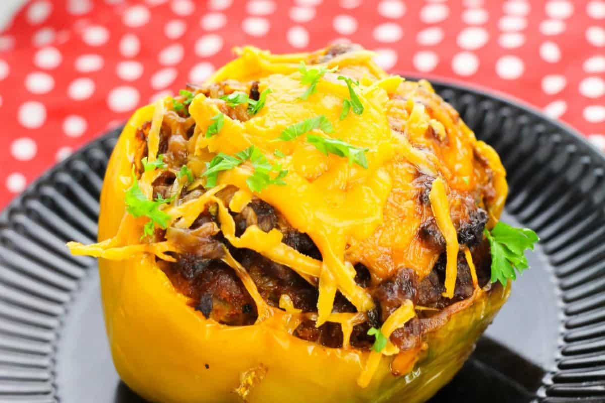A yellow bell pepper stuffed with ground meat and beans, topped with melted cheddar cheese and parsley—an easy stuffed peppers recipe perfect for a quick weeknight dinner, served on a black plate.