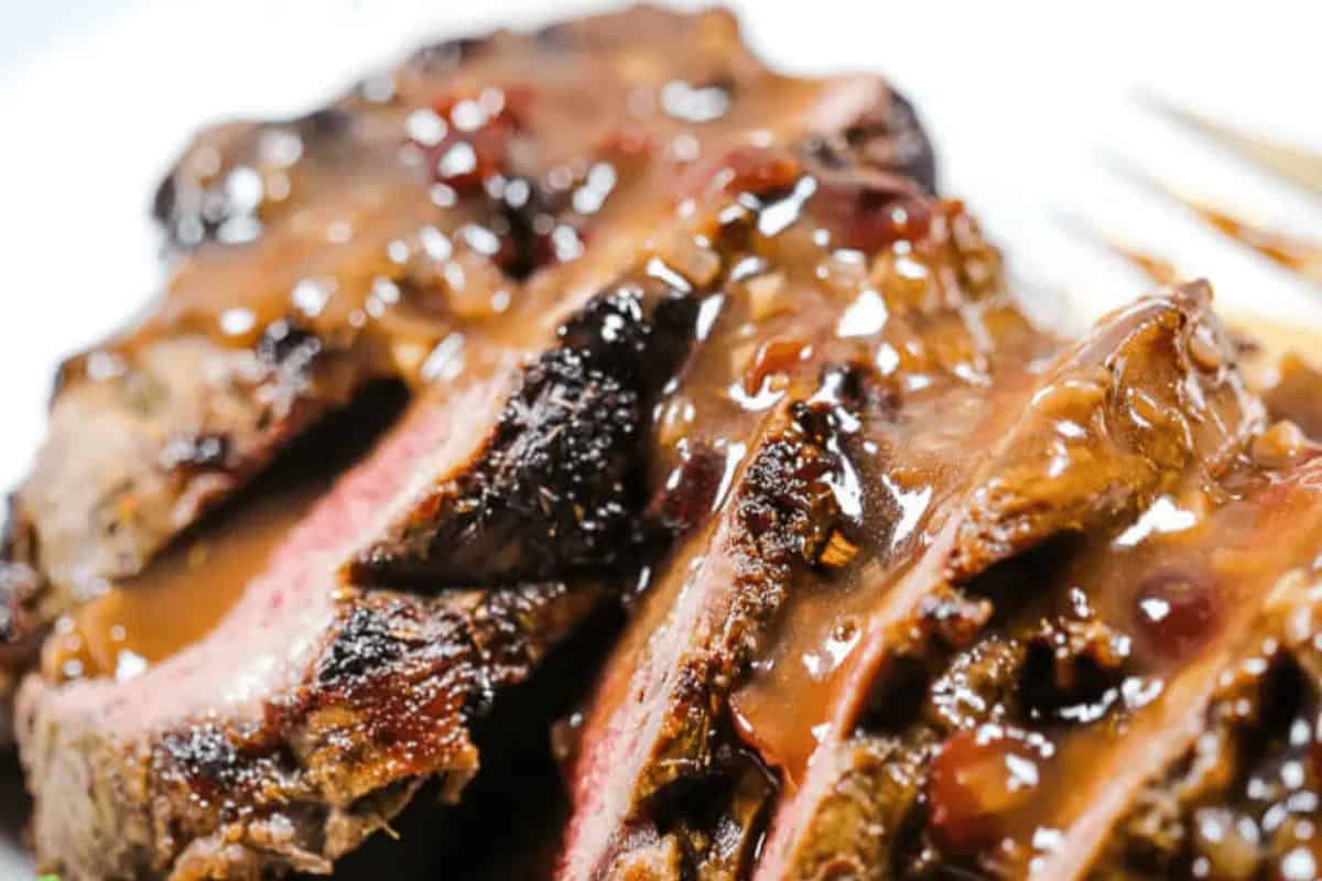 Sliced beef roast topped with port wine sauce, showcasing a seared exterior and pink interior, served on a white plate