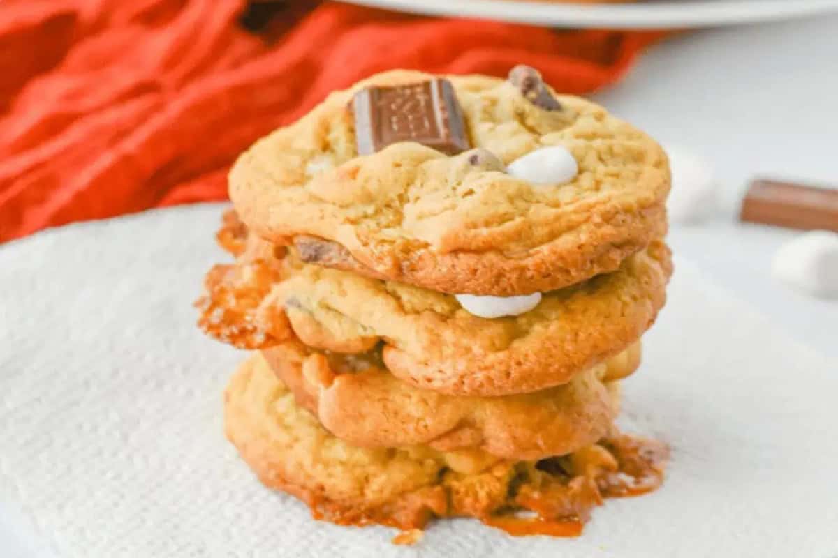 A stack of three Christmas Smores cookies with melted chocolate and marshmallows sits on a white napkin.