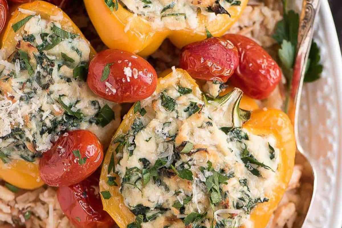 Close-up of easy stuffed peppers: yellow bell peppers filled with a spinach and cheese mixture, served with roasted cherry tomatoes and fresh herbs on a bed of rice—perfect for tasty weeknight dinners.