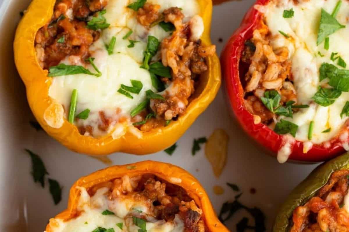 Three stuffed bell peppers—yellow, red, and green—filled with rice, meat, tomato sauce, and melted cheese, topped with fresh herbs. Perfect for easy stuffed peppers or weeknight dinners.