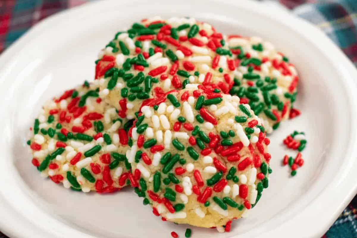 A plate of Christmas cookies topped with red, green, and white sprinkles, arranged on a white dish for a cozy Christmas treat.