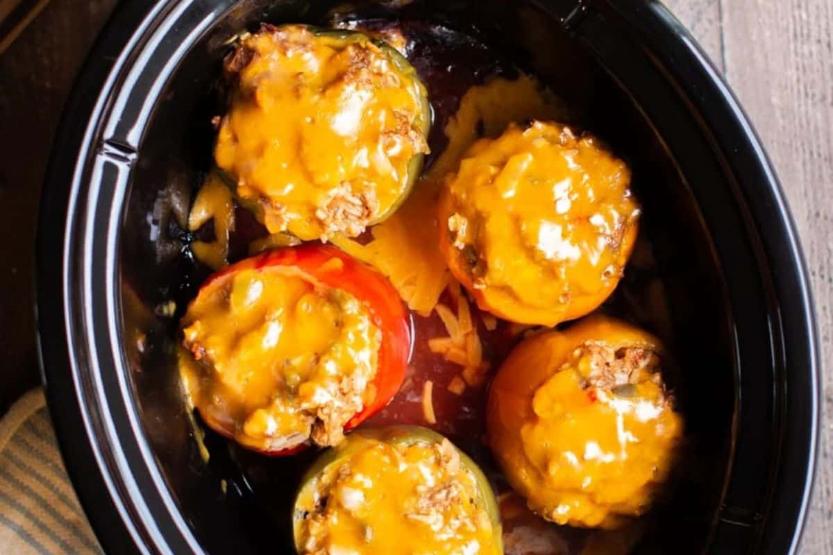 Five easy stuffed peppers topped with melted cheddar cheese inside a black slow cooker—perfect for effortless weeknight dinners.