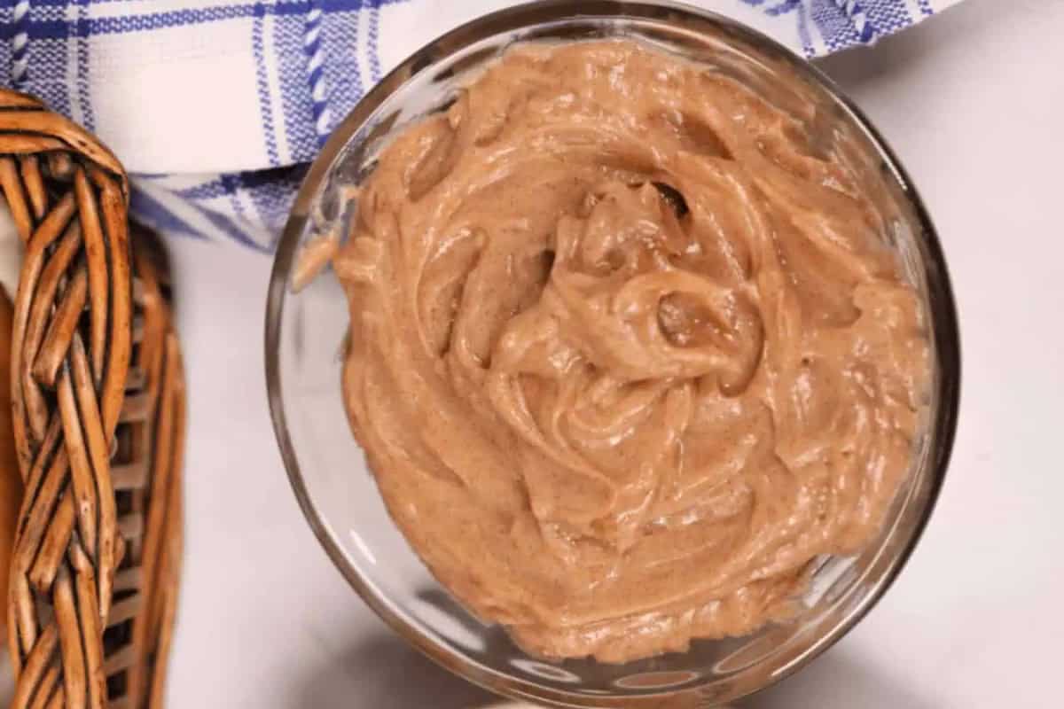 A glass bowl filled with swirled Texas Roadhouse cinnamon butter sits on a white surface next to a wicker basket and a blue-and-white checkered cloth.