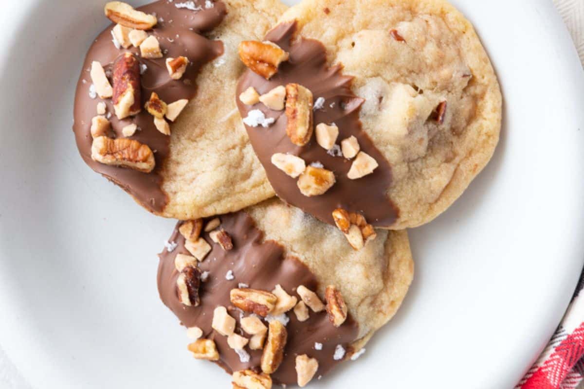 Golden brown cookies packed with chopped pecans and toffee bits, served on a white plate.