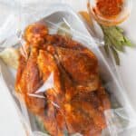 An oven bird on a baking tray with halved garlic, bay leaves, and a small bowl of spice mix on the side.