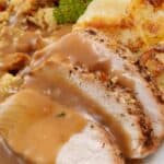 Sliced roast turkey with Turkey Gravy from the Drippings, scalloped potatoes, stuffing, and a parsley garnish on a white plate.