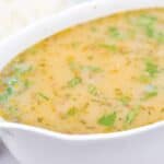 A close-up of a white bowl filled with creamy, herb-flecked Turkey Gravy without Turkey Drippings, garnished with chopped parsley.