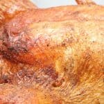 Close-up of a whole roasted chicken with crispy, golden-brown skin, reminiscent of turkey in the roaster oven, resting on a black surface.