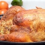 A close-up of Turkey in the Roaster Oven shows browned, crispy skin and stuffing, set against a background with tomatoes and a green pepper.