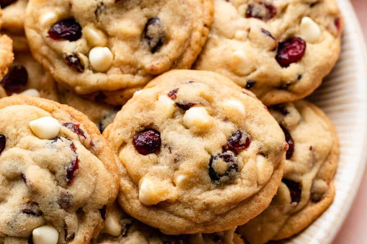Soft-baked cookies filled with dried cranberries and white chocolate chips on a white serving tray.