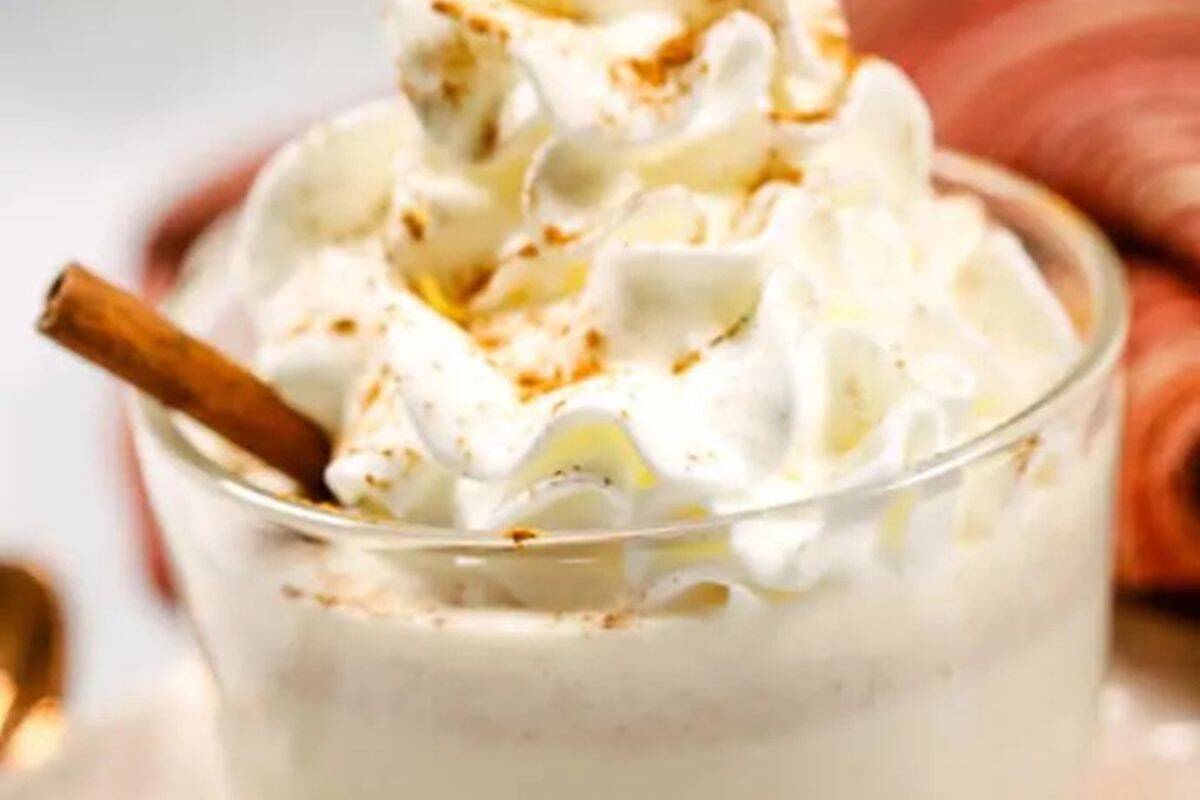 A glass of white hot chocolate  topped with whipped cream, sprinkled with cinnamon, and garnished with a cinnamon stick—perfect for those who love warm drinks or creamy hot chocolate.