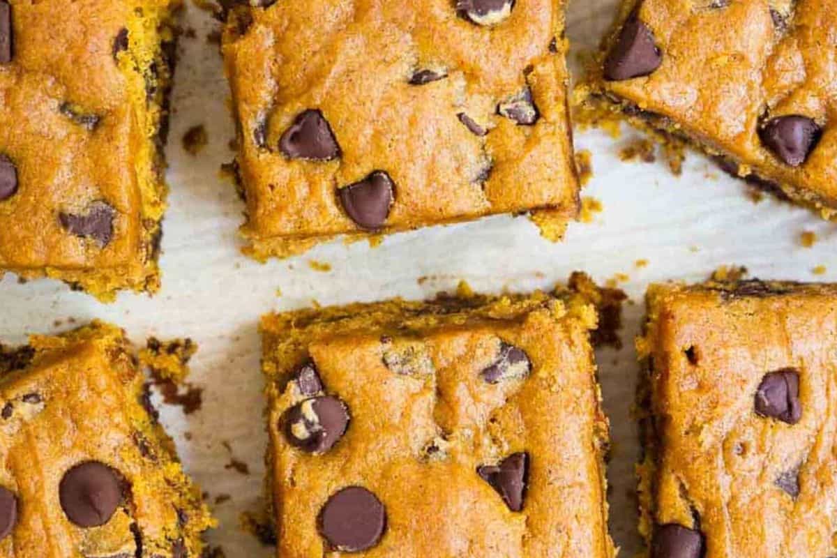 Squares of pumpkin chocolate chip bars arranged on parchment paper, with visible chocolate chips scattered on each bar—perfect for cozy fall vibes and lovers of pumpkin desserts.