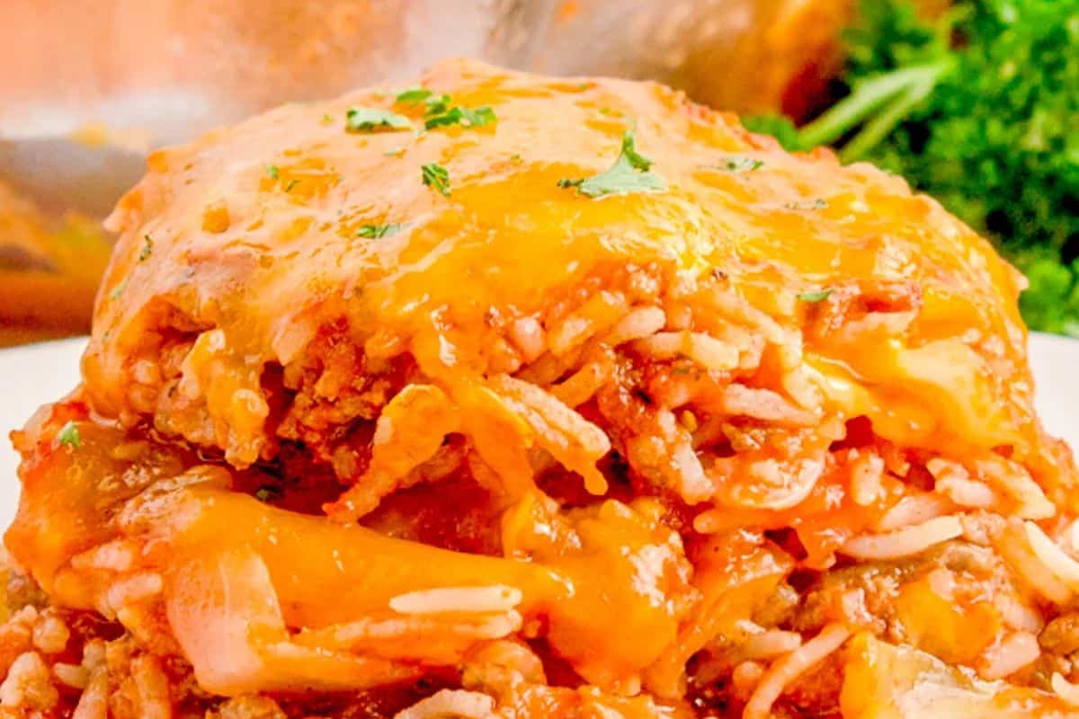 Close-up of a cheesy casserole with ground beef, rice, tomato sauce, and melted cheddar cheese, garnished with chopped parsley—a good casserole to enjoy during cooler weather.