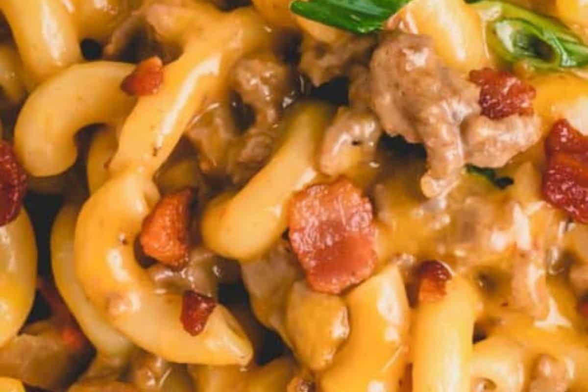 Close-up of creamy pasta with ground meat, melted cheese, and pieces of bacon, garnished with a green herb—a comforting dish perfect for cooler weather and fans of hearty casserole recipes.