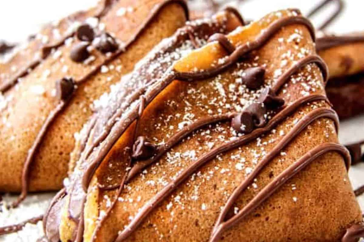 Two folded crepes are topped with a drizzle of chocolate sauce, chocolate chips, and a dusting of powdered sugar—perfect for cozy fall vibes and lovers of pumpkin desserts.