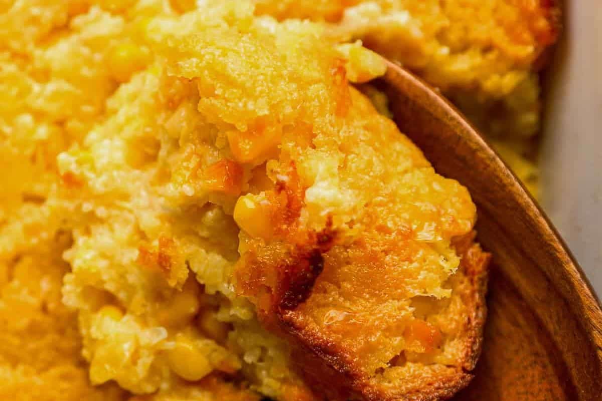 Close-up of a serving of golden brown corn casserole being scooped out with a wooden spoon—a perfect addition to your collection of good casserole recipes for cooler weather.