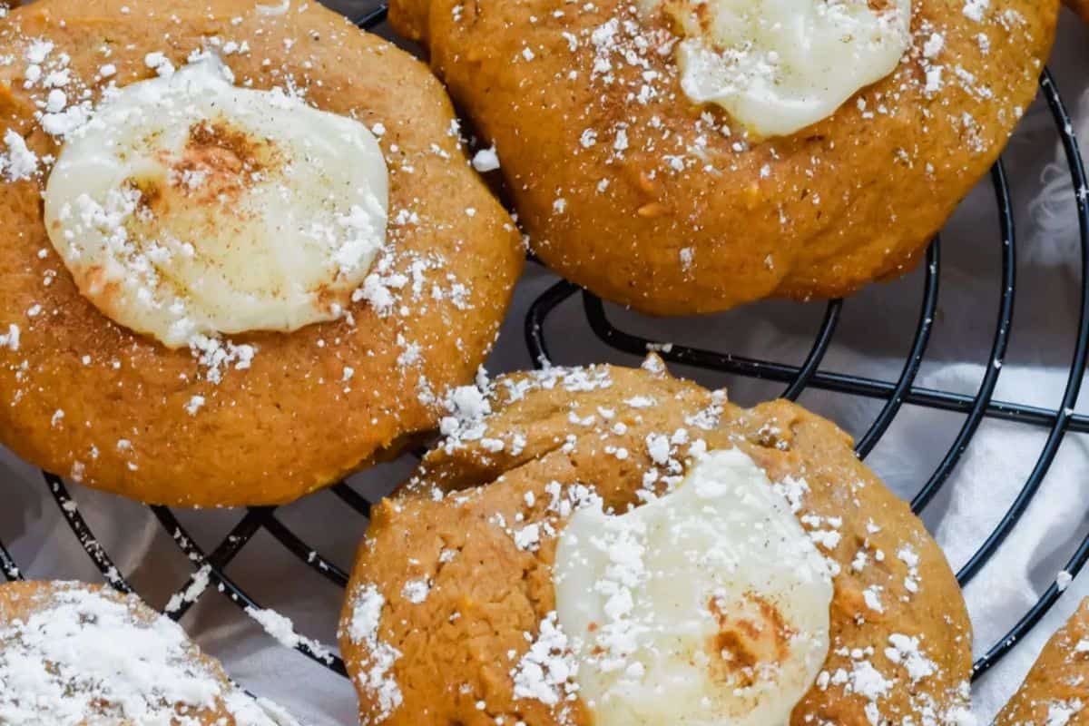 Close-up of cozy pumpkin cookies with cream cheese centers, dusted with powdered sugar, on a black wire cooling rack—perfect for those fall vibes and pumpkin dessert cravings.