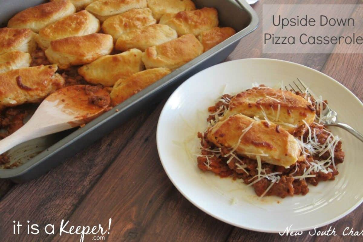 A plate with upside down pizza casserole topped with shredded cheese sits next to a baking pan filled with more casserole and a wooden spatula—perfect for cooler weather and fans of comforting casserole recipes.