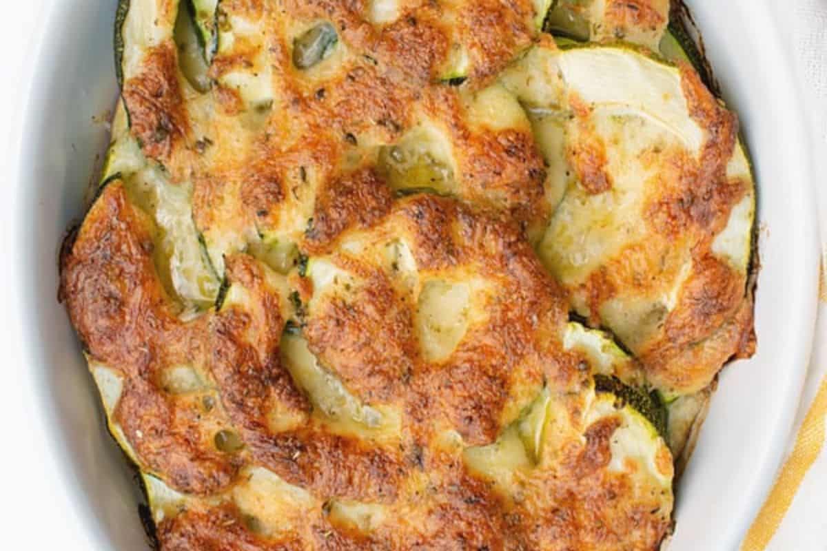 Baked zucchini casserole topped with melted, golden-brown cheese in a white oval dish—a perfect choice for cooler weather and fans of good casserole recipes.