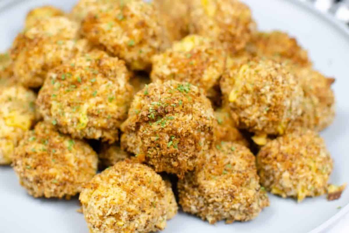 A pile of crispy, golden-brown, breaded mac & cheese bites on a plate, garnished with chopped green herbs, perfect for your Game Day Party.