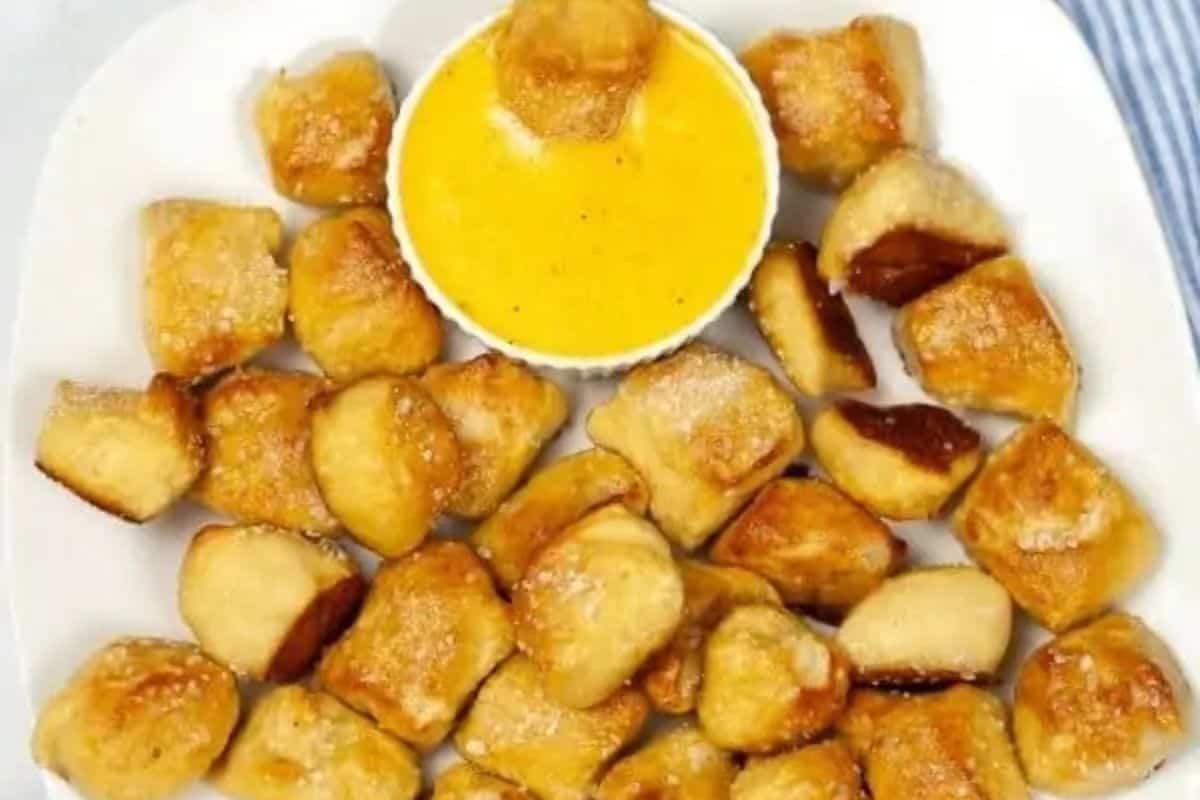 Bite-sized pretzel pieces arranged around a small bowl of yellow cheese dip on a white plate make for perfect game day party snacks.
