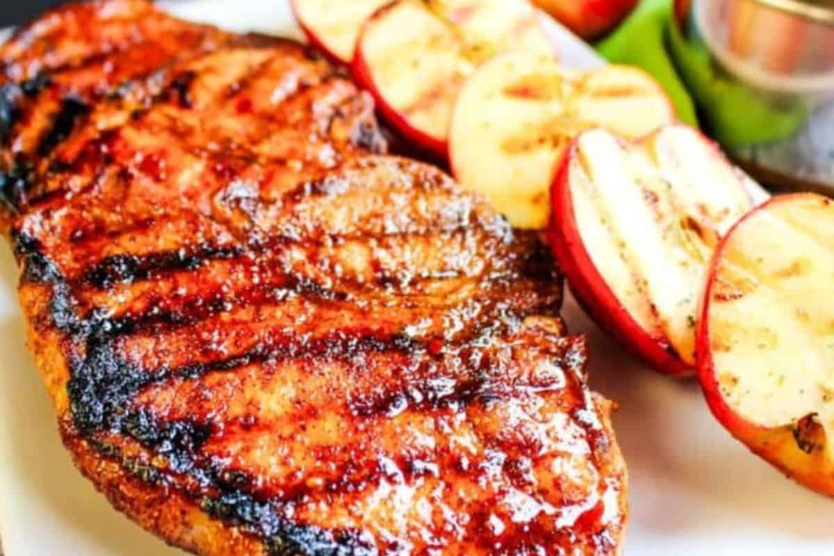 Grilled pork chop coated in a glossy apple cider glaze, served with grilled apple slices on a white plate.