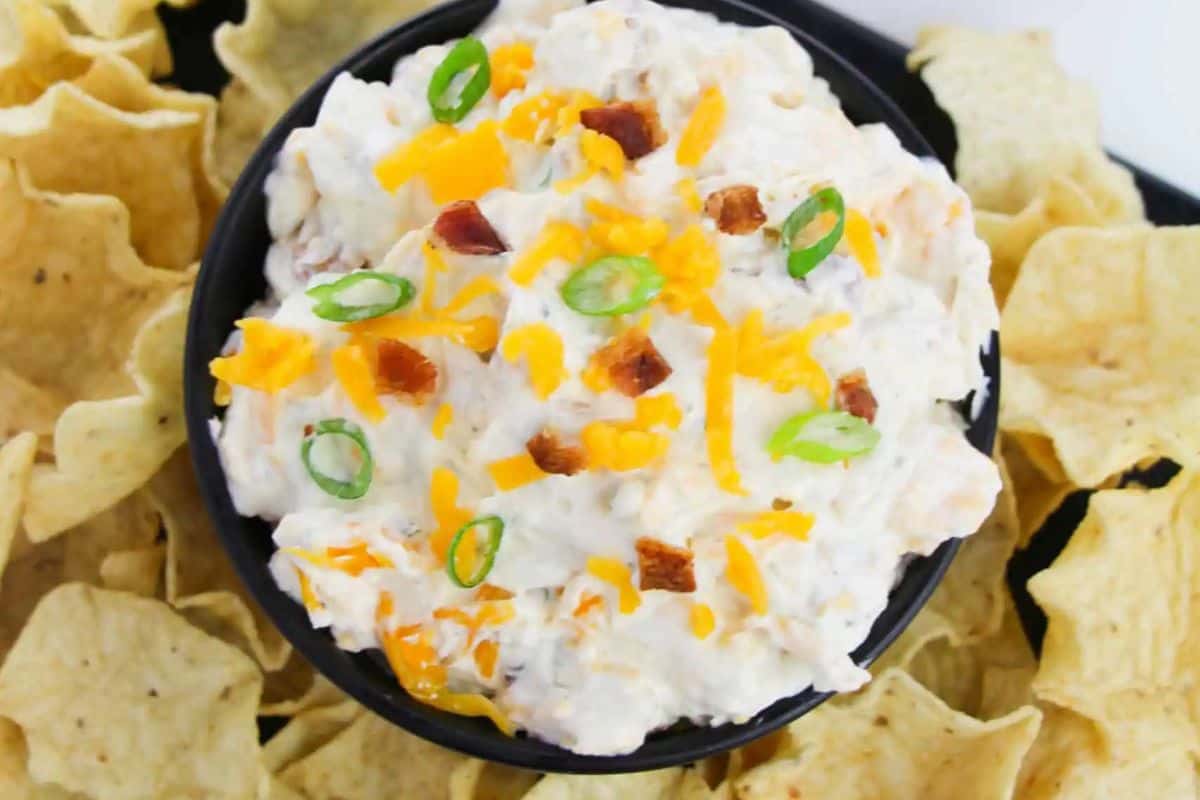 Score big points at your Super Bowl party with a bowl of creamy dip topped with shredded cheese, bacon bits, and sliced green onions, all perfectly surrounded by crispy tortilla chips.