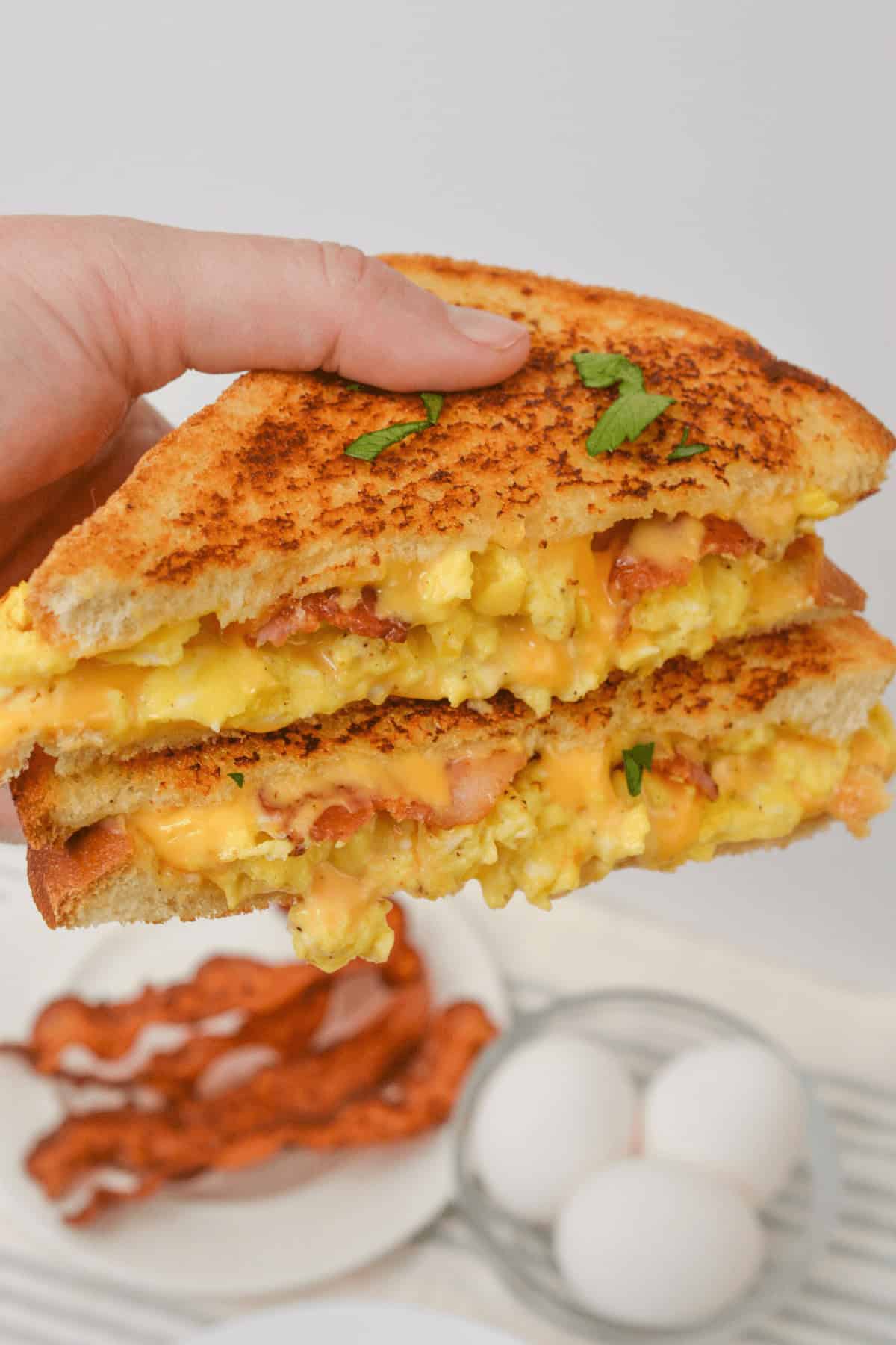 A hand holds a towering breakfast sandwich.