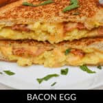 A delicious Bacon Egg and Cheese Grilled Cheese sandwich is cut in half and placed on a white plate, garnished with green herbs.