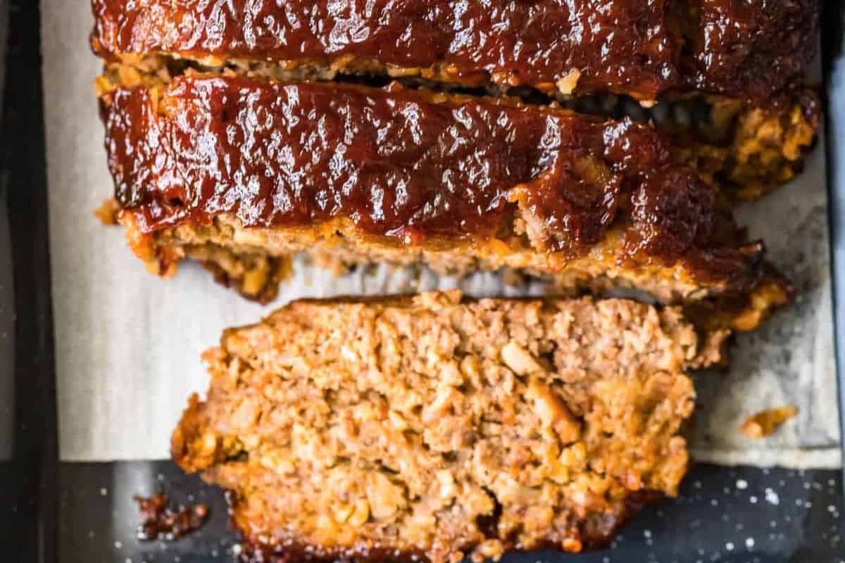 Thick slices of meatloaf speckled with chopped bacon, served on a white plate with a drizzle of glaze.