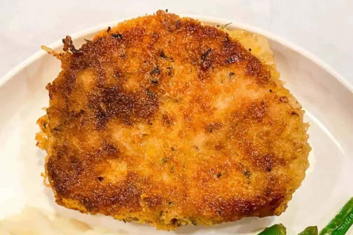 Golden-brown breaded pork chop with a crispy crust, resting on a white plate with green beans partially visible.
