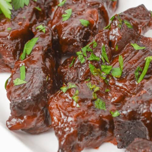 Country style beef ribs garnished with chopped parsley rest enticingly on a pristine white plate.