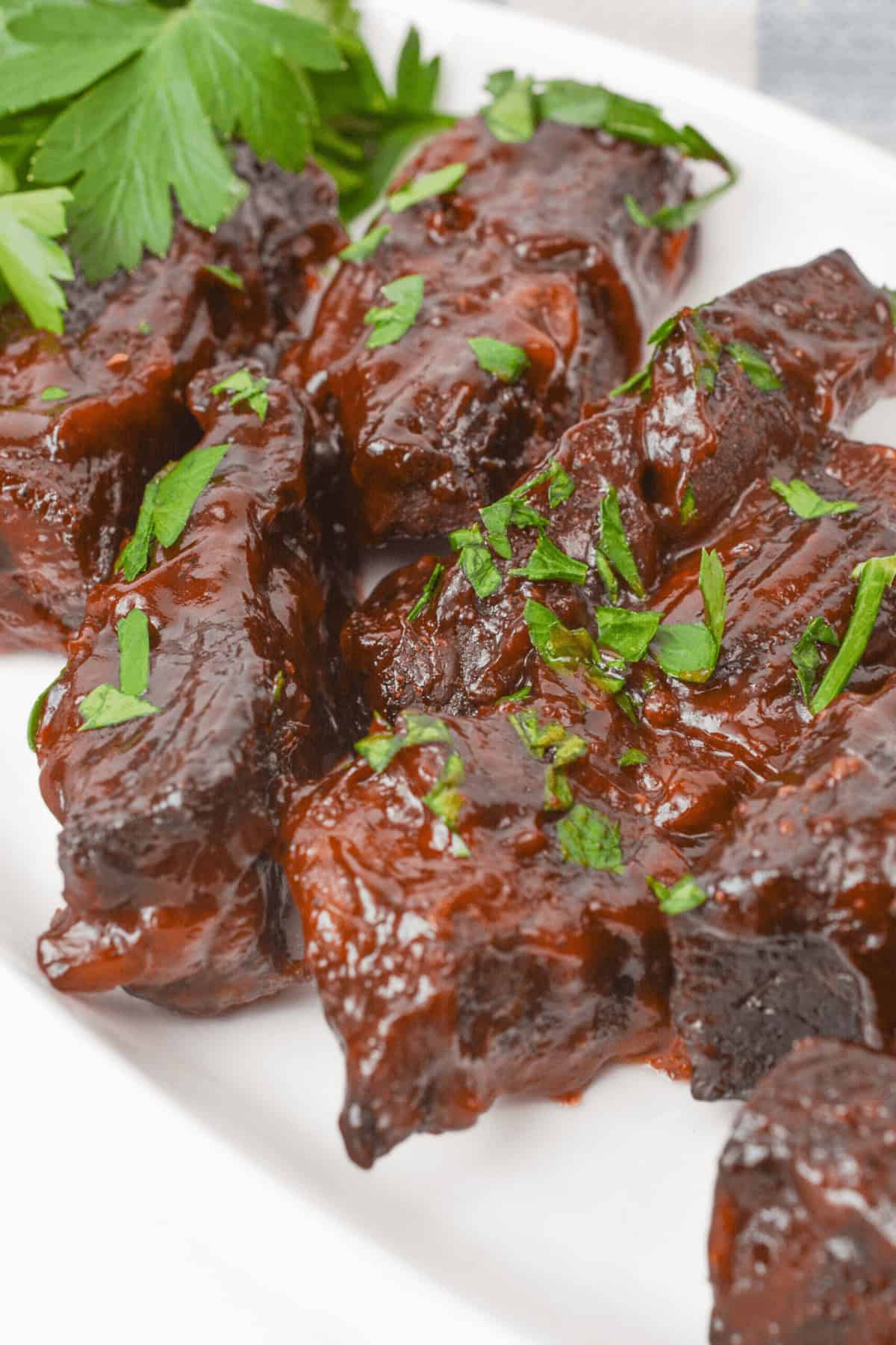 Country style beef ribs garnished with chopped parsley rest enticingly on a pristine white plate.