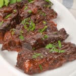 A plate of glazed country style beef ribs garnished with chopped parsley, placed on a white platter.