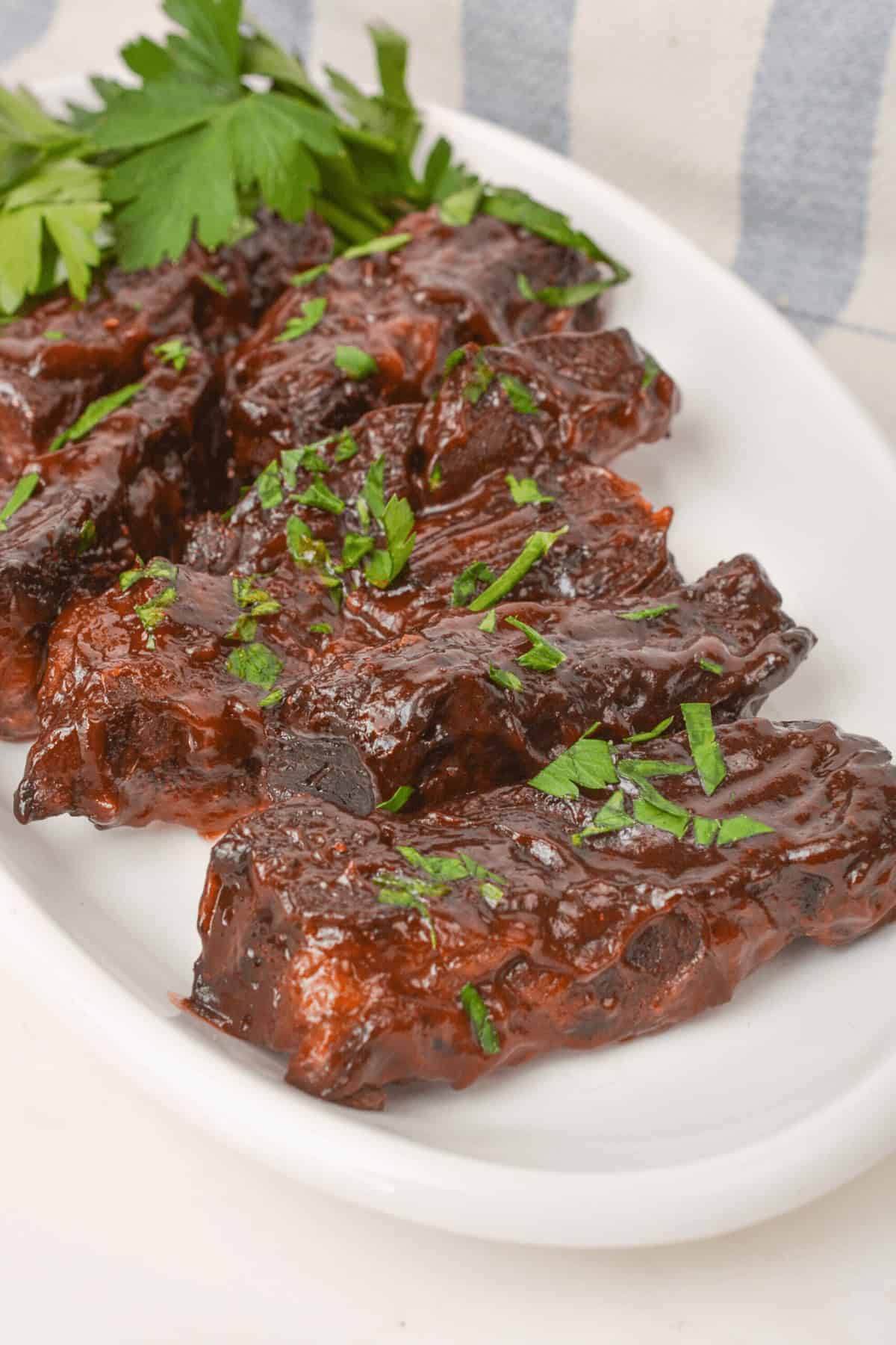 A plate of glazed country style beef ribs garnished with chopped parsley, placed on a white platter.
