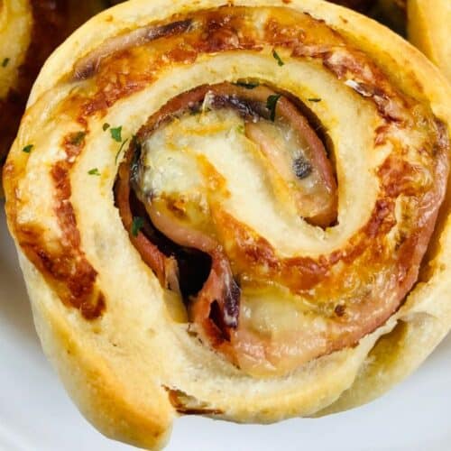 Close-up of a baked pinwheel pastry with visible layers of cheese and ham on a white plate, perfect for your Game Day Party.