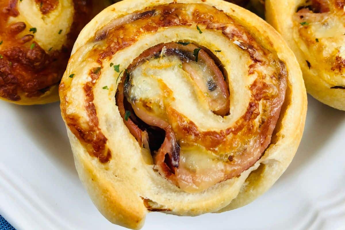 Close-up of a baked ham and cheese roll up with visible layers of cheese and ham on a white plate, perfect for your Game Day Party.