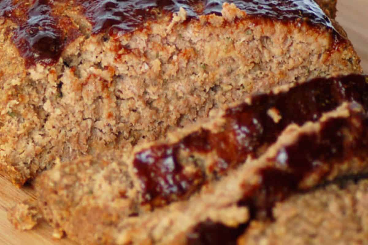 Glazed meatloaf with a shiny balsamic finish, sliced on a cutting board and garnished with herbs.