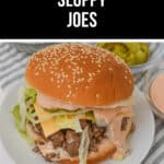 A Big Mac Sloppy Joe with lettuce, cheese, and sauce on a sesame seed bun sits on a plate, accompanied by pickles and extra sauce in small bowls for that perfect bite.