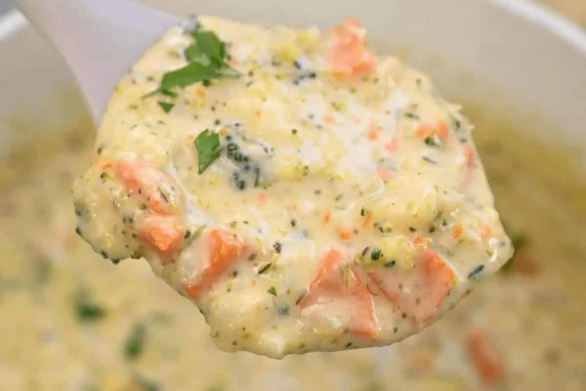 A close-up of a spoonful of creamy soup with visible chunks of broccoli, carrot, and herbs, held above a bowl—perfect for those seeking cozy vegetable soups to warm up on chilly days.