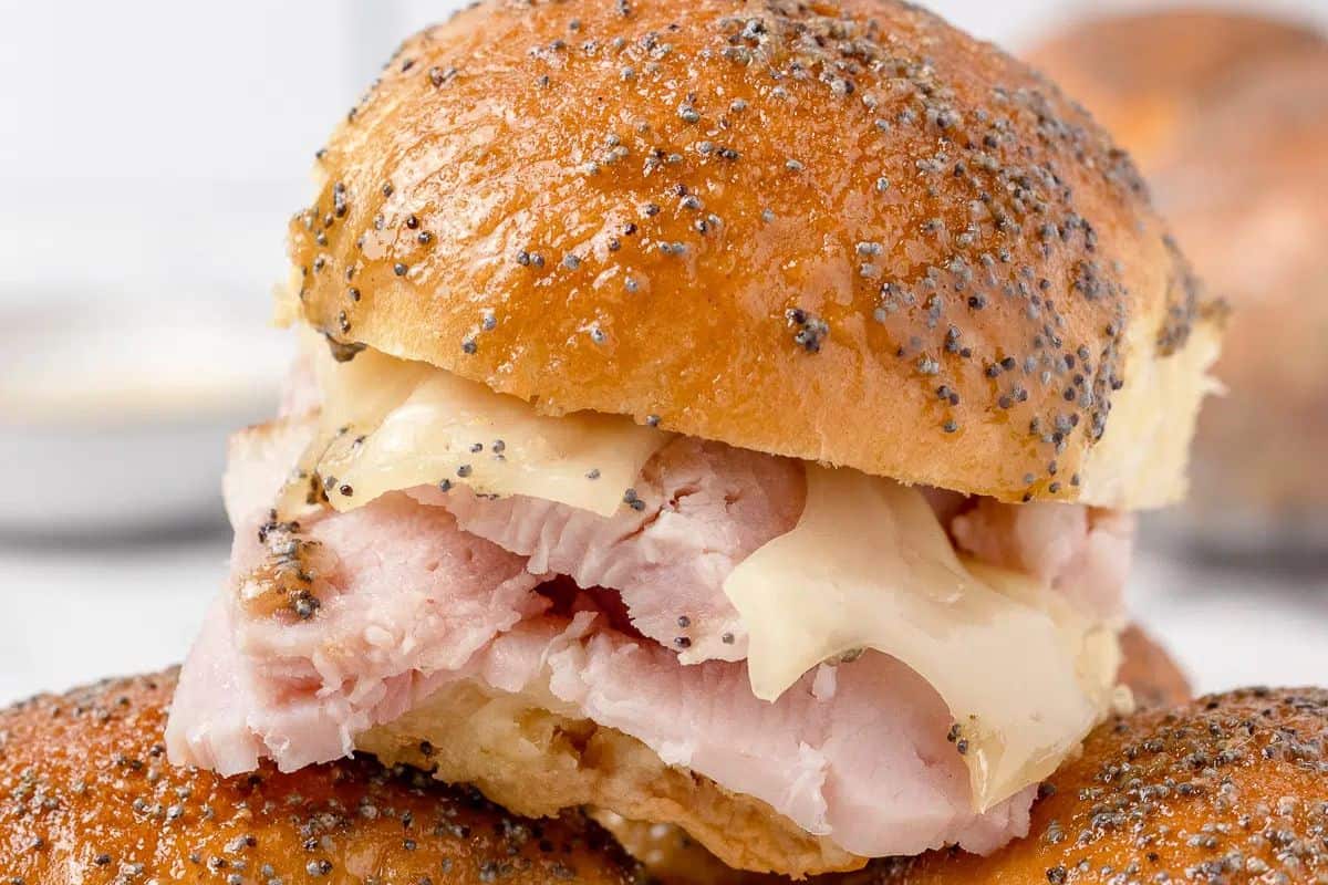 Close-up of an irresistible slider with sliced brwon sugar ham and cheese inside a poppy seed topped bun, perfect for Game Day.