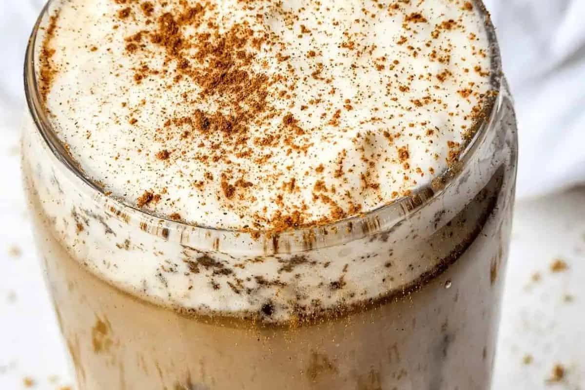 A close-up of a glass filled with iced coffee, topped with frothy cream and sprinkled with ground cinnamon—recreate this Starbucks drink at home for a café-worthy treat.