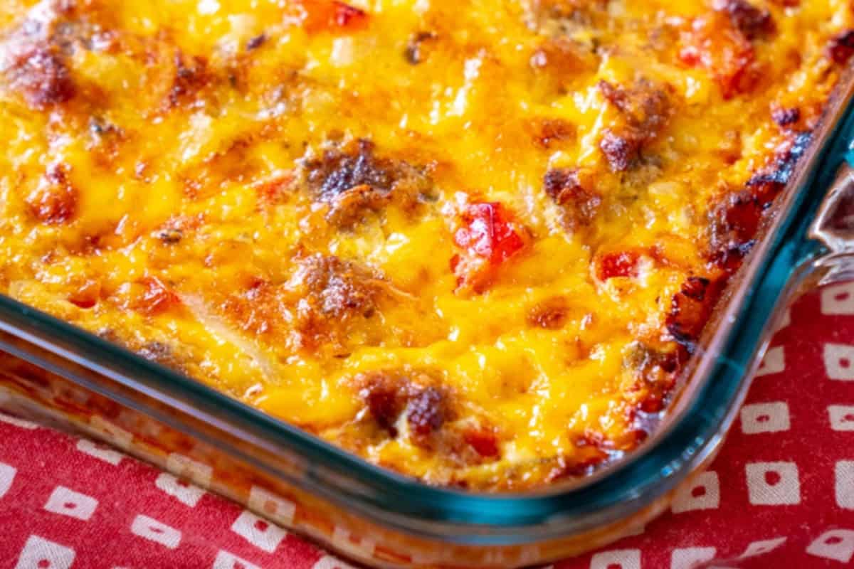 A close-up of a baked casserole with melted cheese, browned edges, and visible pieces of sausage and red bell pepper in a glass dish—perfect for weekend brunch or lazy morning recipes.