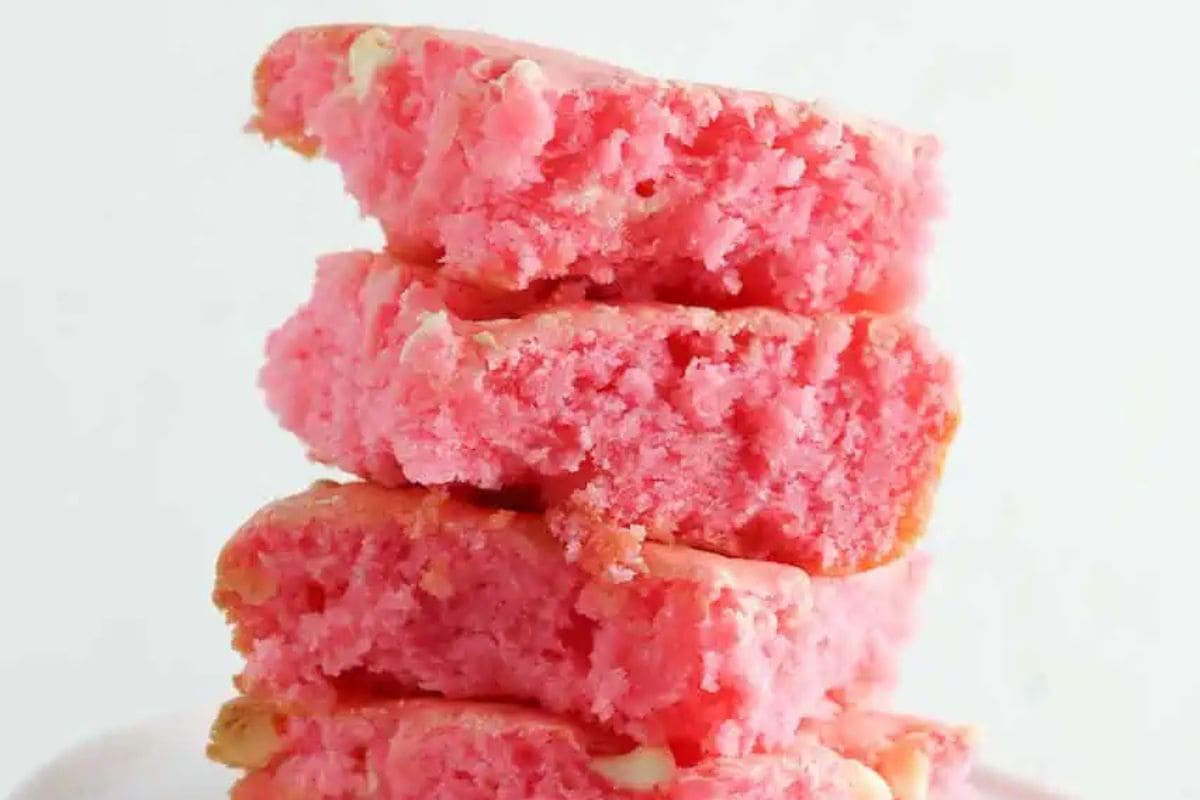 A stack of four pink cake slices with a crumbly texture, against a plain white background, offers perfect Valentine dessert ideas to wow your sweetheart.
