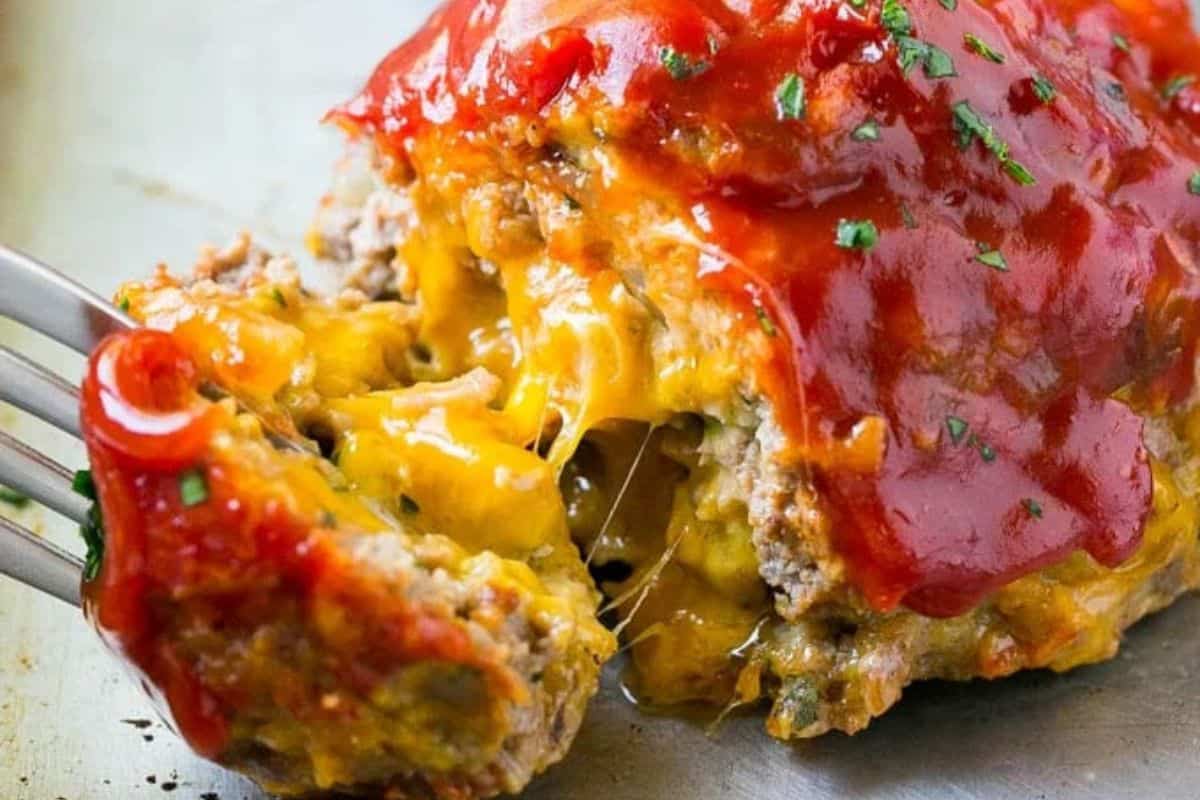 Cheeseburger-inspired meatloaf topped with melted cheese and chopped pickles, sliced and ready to serve.
