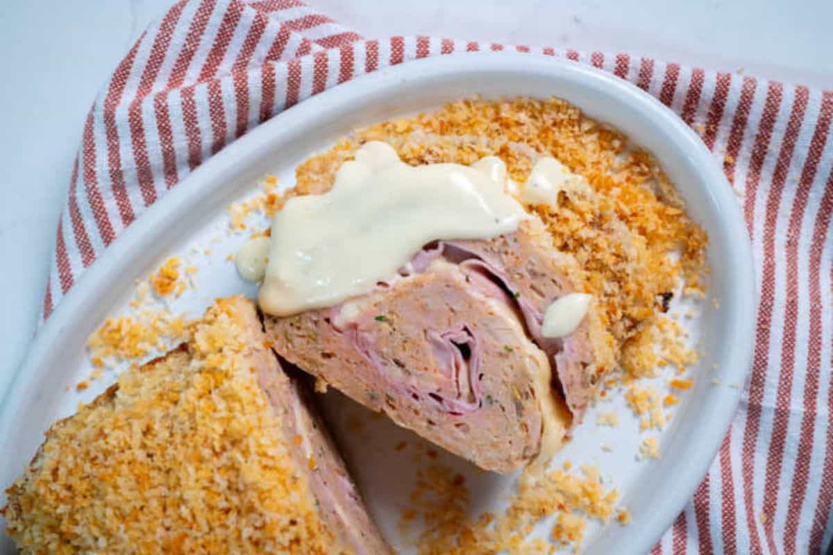 Sliced chicken cordon bleu meatloaf revealing layers of ham and melted Swiss cheese inside.