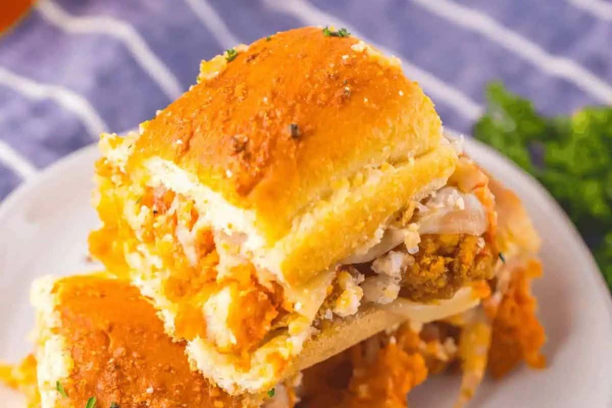 Irresistible game day is made perfect with these two stacked cheesy chicken parm sliders, drizzled with savory sauce and garnished with fresh herbs on a white plate.